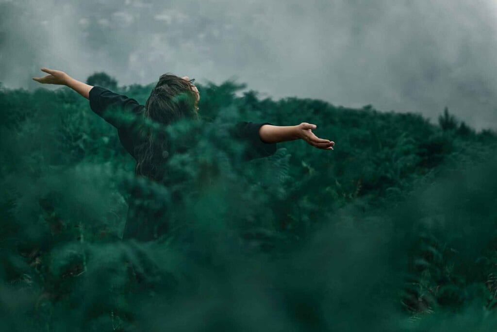 Silhouette with arms raised in a forest, expressing freedom and peace.